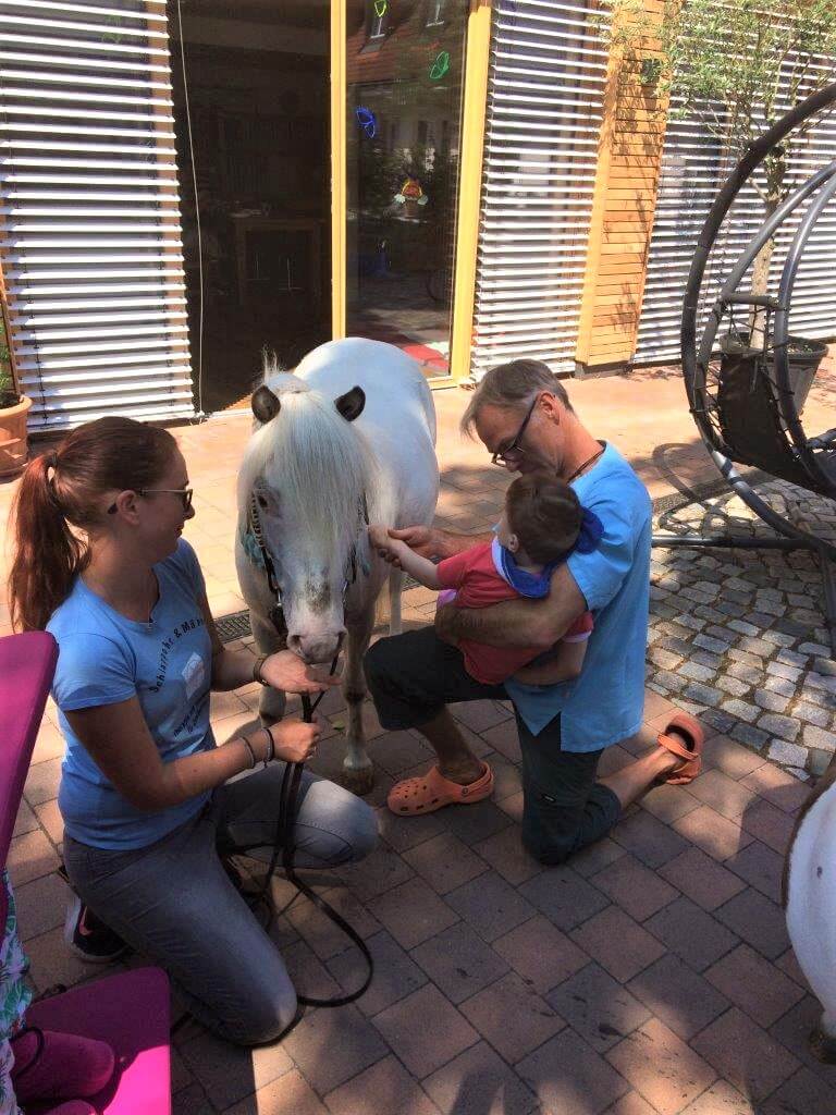 Ein Heilerziehungspfleger streichelt mit dem Kind ein Pony.